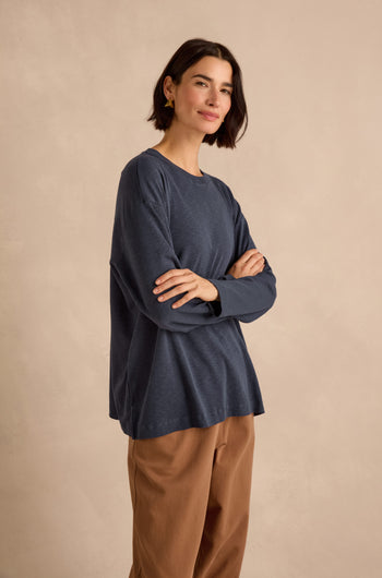 A woman with short dark hair stands with arms crossed against a neutral background, wearing a Navy Boxy Cotton Jersey T Shirt and tan pants.