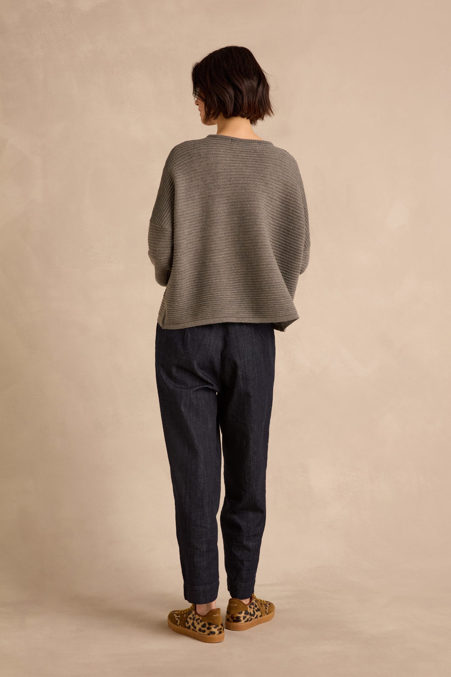 A person stands with their back to the camera, wearing the Mole Fine Rib Merino Top paired with dark pants and leopard print shoes, set against a beige background.