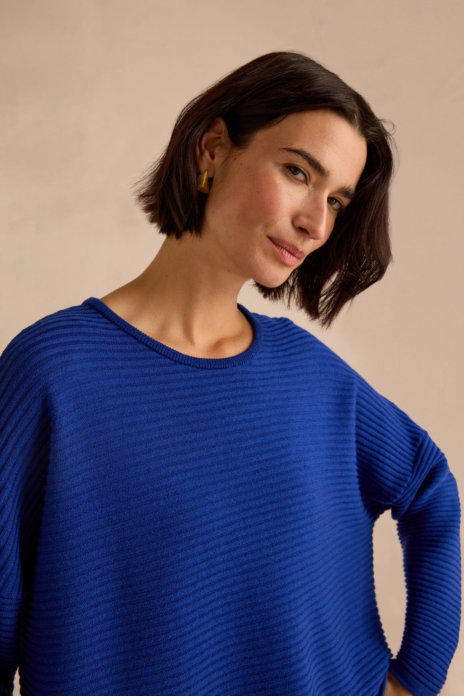 A woman with short dark hair wears the Royal Blue Fine Rib Merino Top in a relaxed, boxy fit. She stands against a plain, light-colored background, gazing slightly to the side.