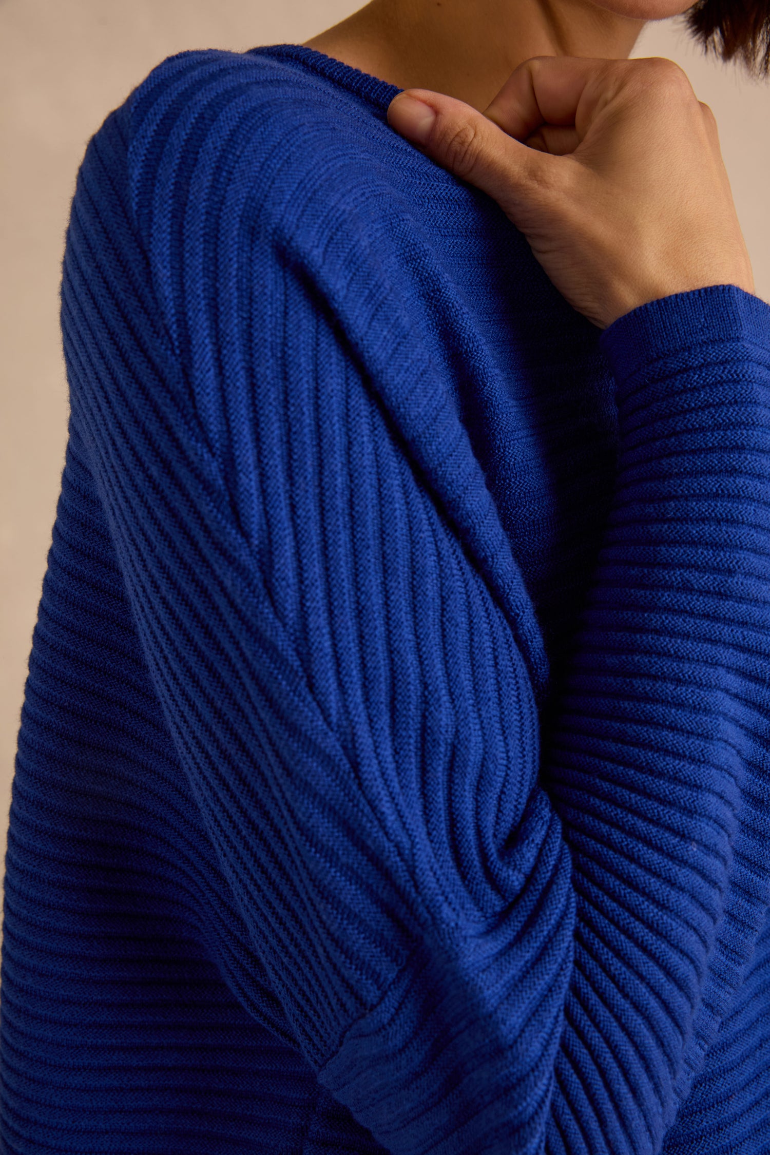 A person wearing the Royal Blue Fine Rib Merino Top—a relaxed, boxy-fit, ribbed merino wool shirt in bright blue—is shown from the upper torso up, with one hand holding the collar near their neck.