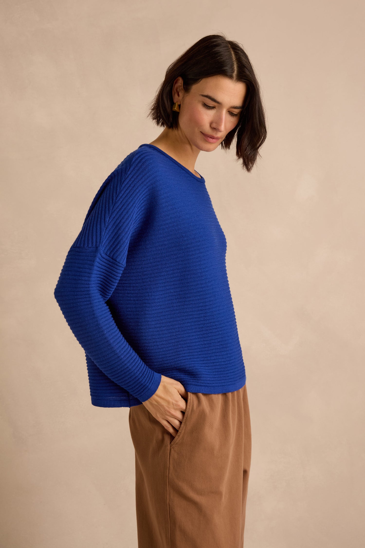 A person wearing the Royal Blue Fine Rib Merino Top in a relaxed boxy fit and tan pants stands against a light beige background, looking slightly downward.
