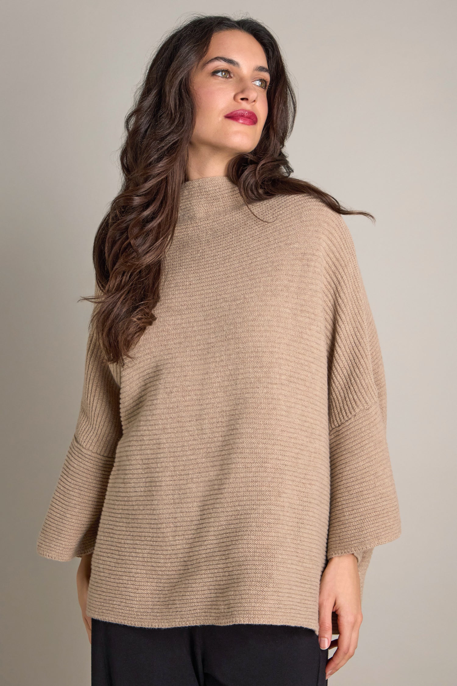 A person with long hair is wearing a beige Pauline Rib Boxy Knit sweater, exuding cozy comfort.