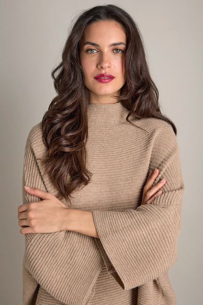 Wearing the cosy Pauline Rib Boxy Knit, a person with long brown hair stands with arms crossed, looking at the camera.