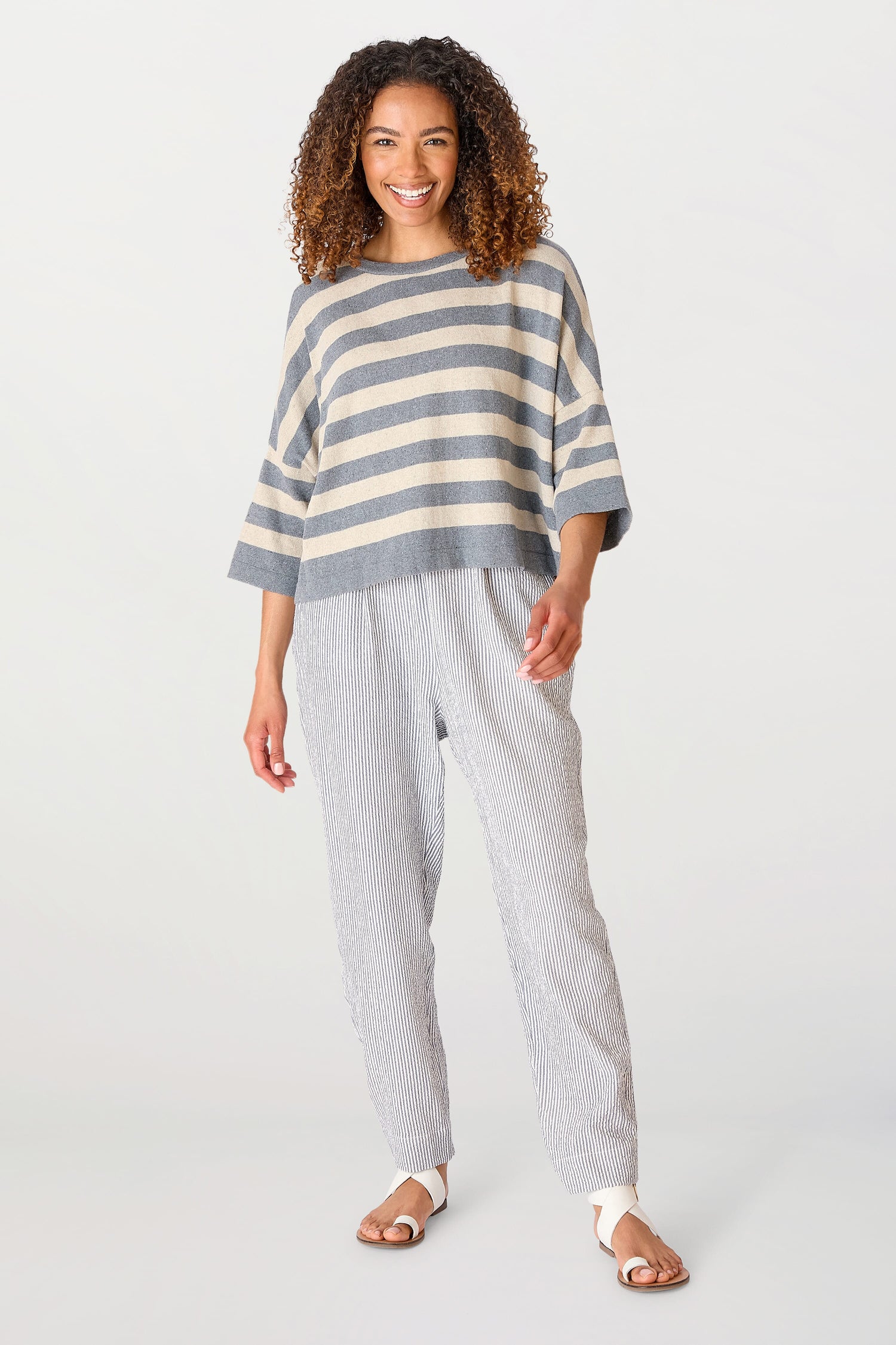 A woman smiling at the camera, wearing a Vibe Stripe Top and striped pants, standing in a white studio.