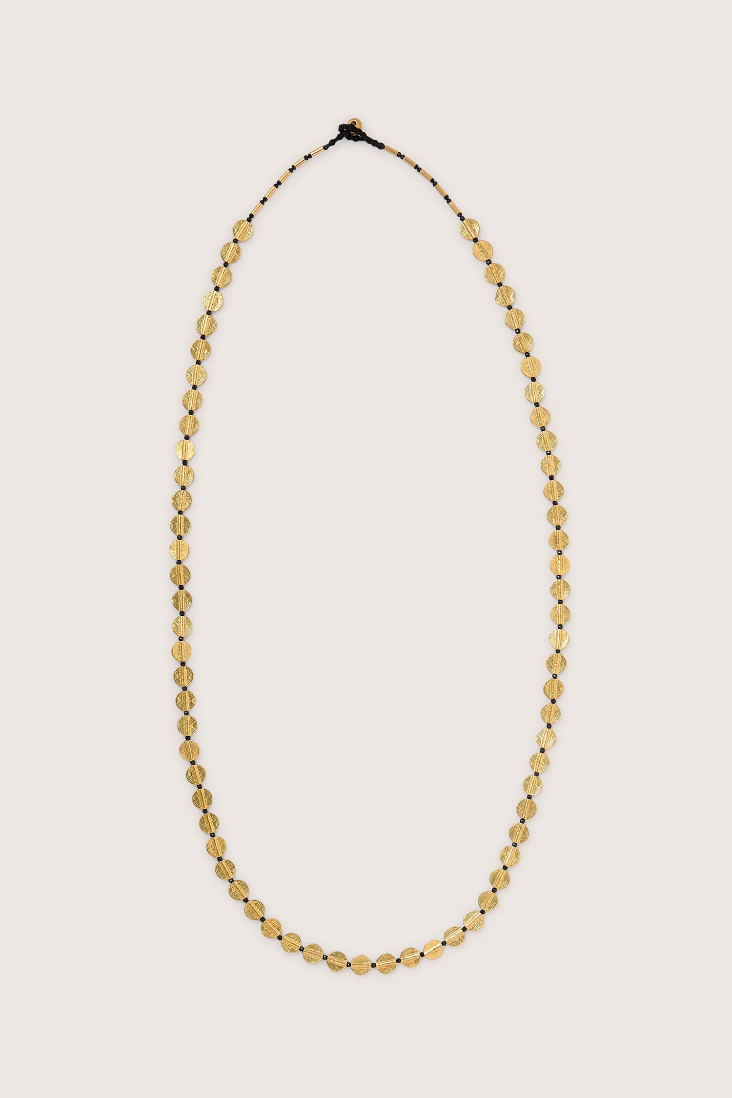 The Engraved Circles Necklace, meticulously crafted by skilled Jaipur artisans, features a series of gold beads interconnected with a secure clasp and is elegantly displayed on a plain background.