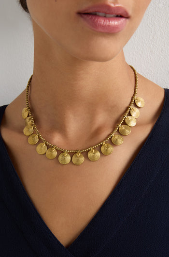A person wearing a Short Gold Chakra Necklace with golden discs and a dark V-neck top, creating a timeless statement.