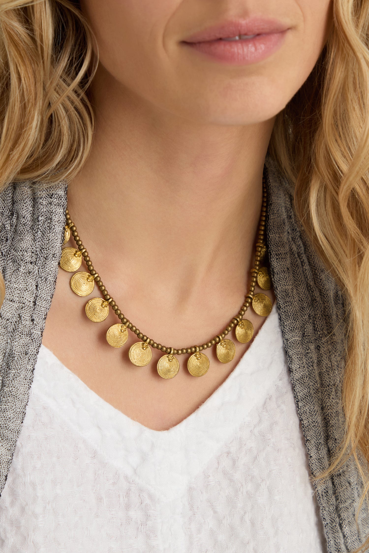 A woman wearing a textured gray jacket, a white V-neck top, and the Short Gold Chakra Necklace.