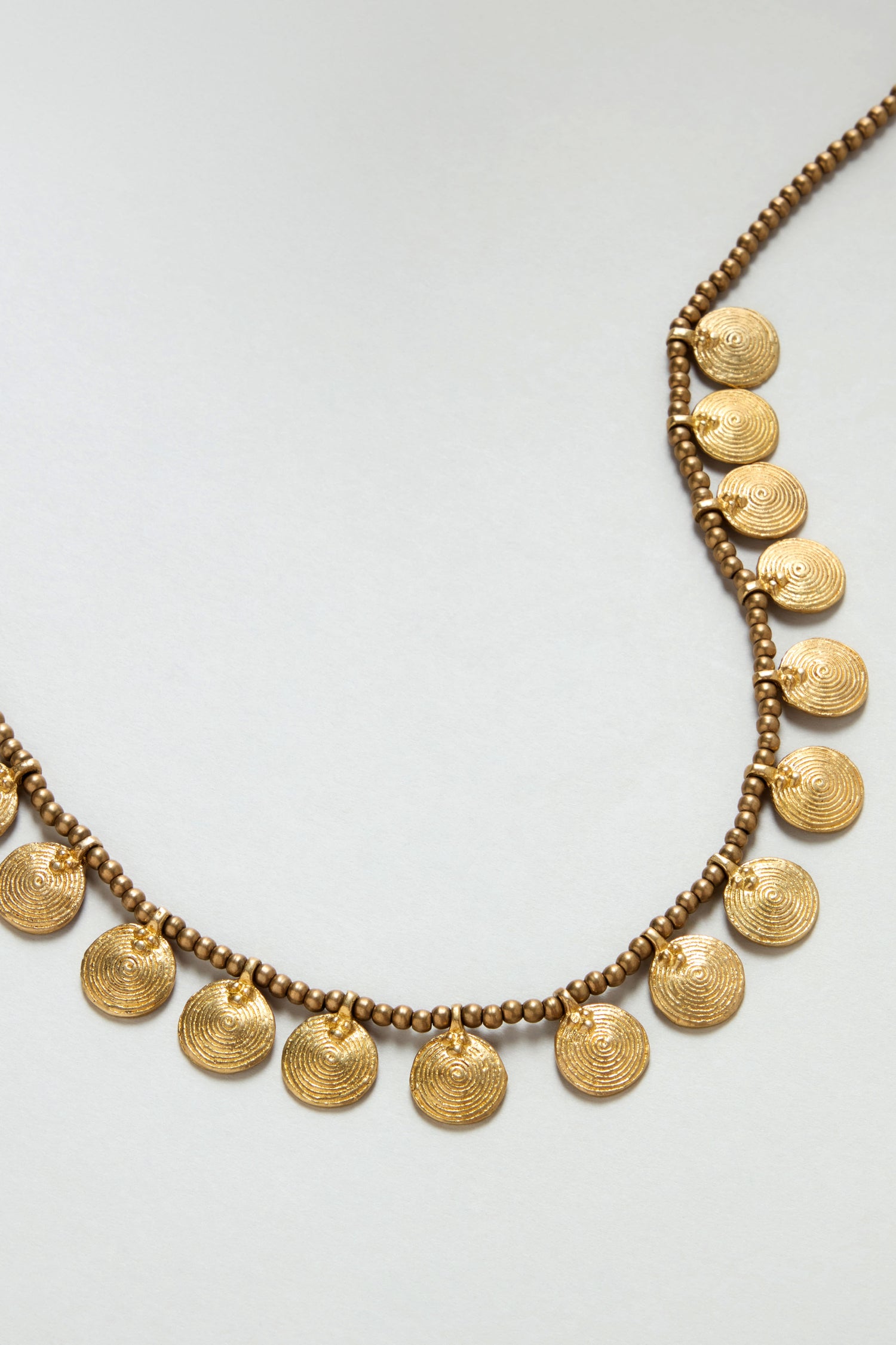 Short Gold Chakra Necklace with evenly spaced round, textured gold-tone coin pendants on a simple light background.