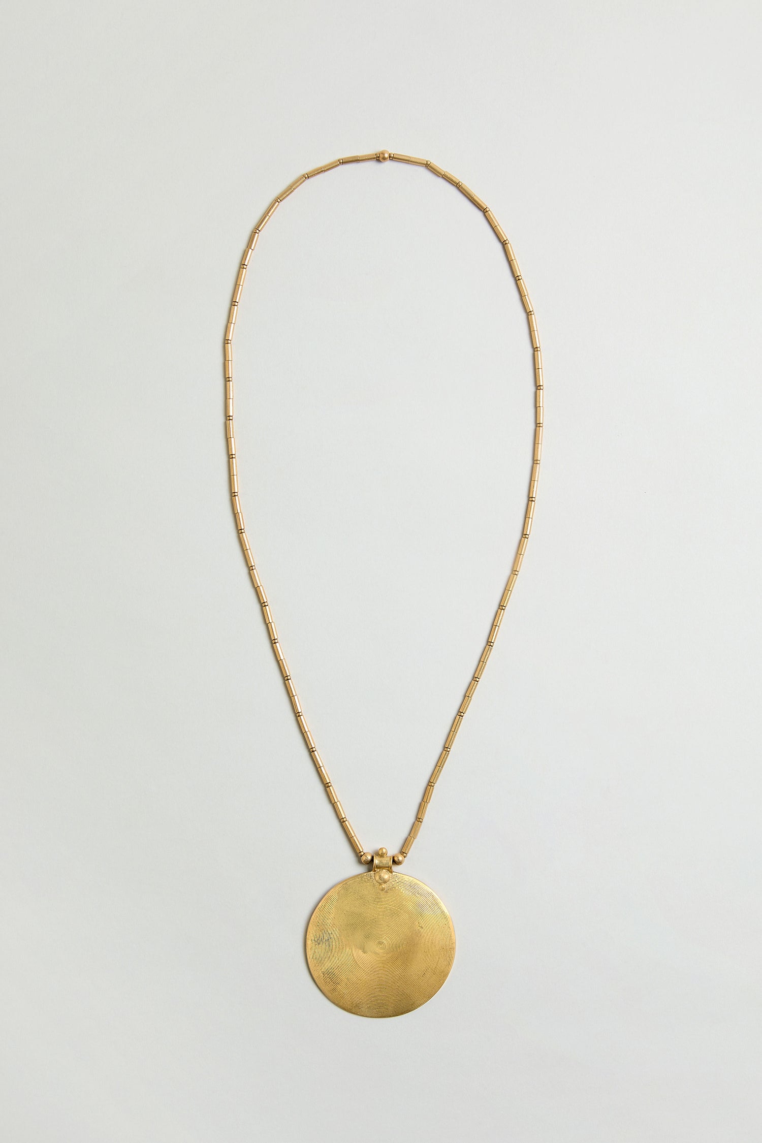 The Long Spiral Pendant features a thin, beaded gold chain with a large, round spiral pendant—ideal for making a statement. Displayed on a light, neutral background.