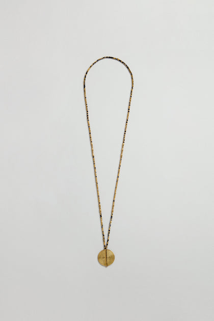 The Long Mini Spiral Bead Pendant is a brass necklace with a thin chain and spiral bead pendant, inspired by handmade Indian jewelry, displayed on a plain white background.