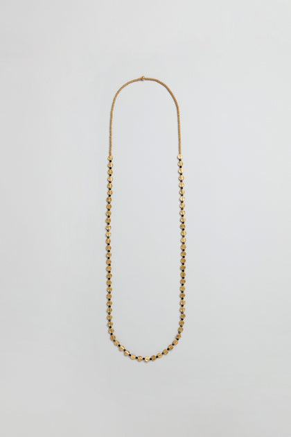 The Mini Engraved Circles Bead Necklace features small, evenly spaced gold oval beads and an elegant engraved disc pendant, displayed on a plain light gray background.