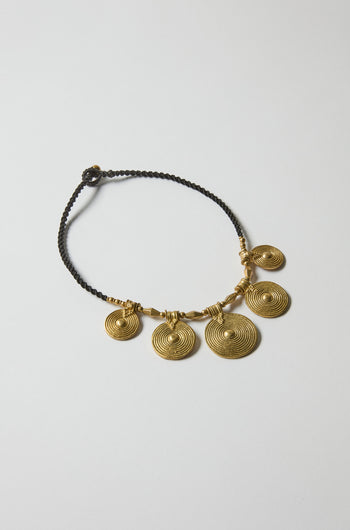 The Elissos Engraved Necklace features five round gold spiral pendants on a black braided cord, showcasing handcrafted style and modern elegance against a plain white background.
