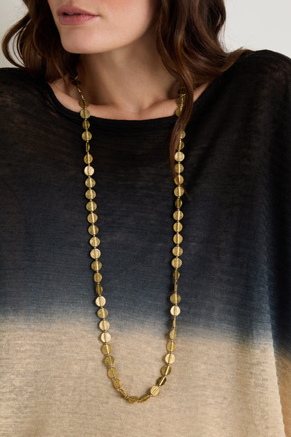 A woman wearing the Long Engraved Circles Necklace over a loose-fitting top with a black-to-beige gradient.