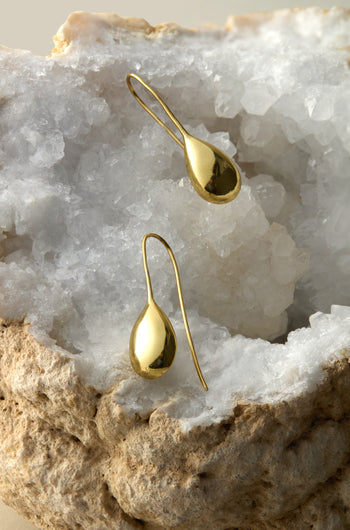 The Gold Gilded Teardrop Earrings shimmer beautifully on a rugged geode with sparkling white crystals, offering an elegant upgrade to your summer style.