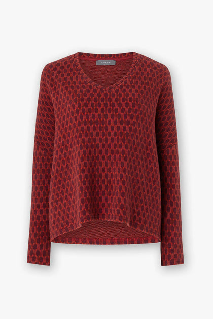 The Honeycomb Top is an oversized red knit sweater with a unique honeycomb pattern, V-neck, and long sleeves set against a white background, highlighting the craftsmanship of Italian artisans.