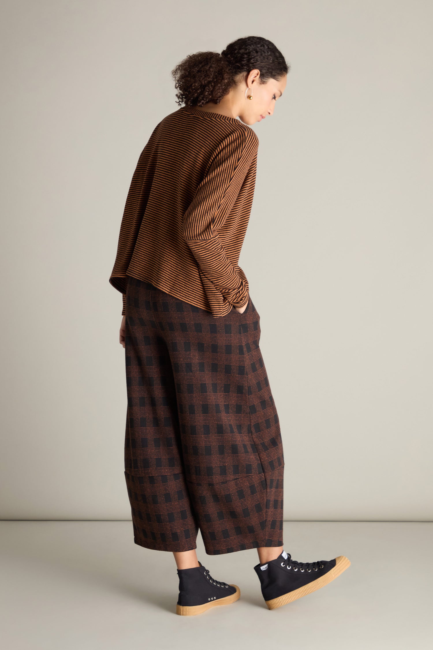 A person wearing a Neirami Mini Stripe Boxy Top in brown stripes and brown plaid wide-leg pants with black high-top sneakers is standing against a plain background. This versatile wardrobe essential offers both comfort and style.