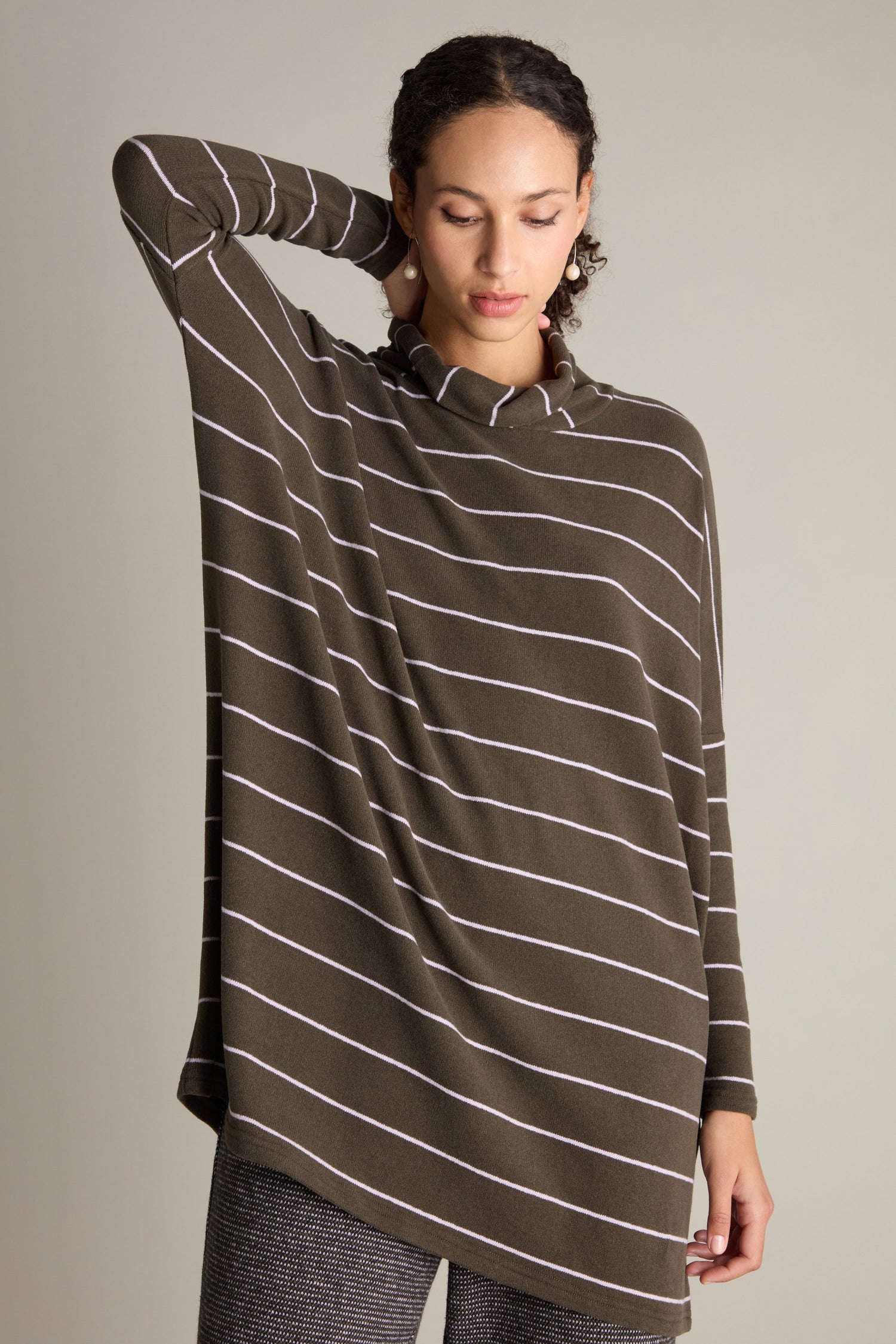 Person standing with one hand behind head, wearing an oversized dark green striped sweater and checkered pants against a plain background. The look is accentuated by the long-length silhouette of the classic Narrow Stripe Polo Tunic seamlessly blending into the outfit.