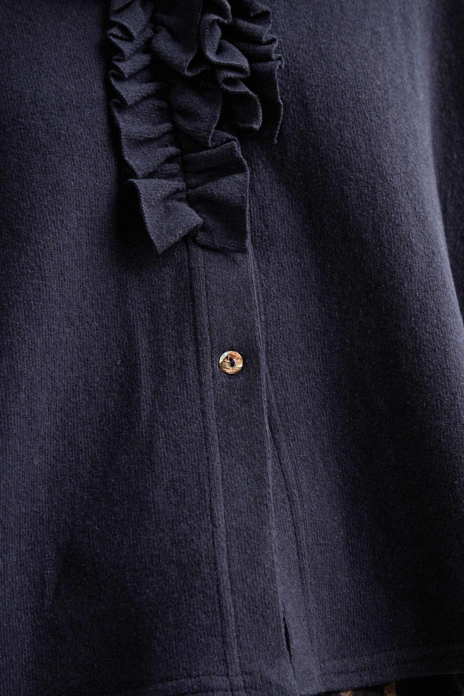 Close-up of the Frill Neck Navy Fleece Cardigan, featuring a single visible button and decorative fabric ruffles.