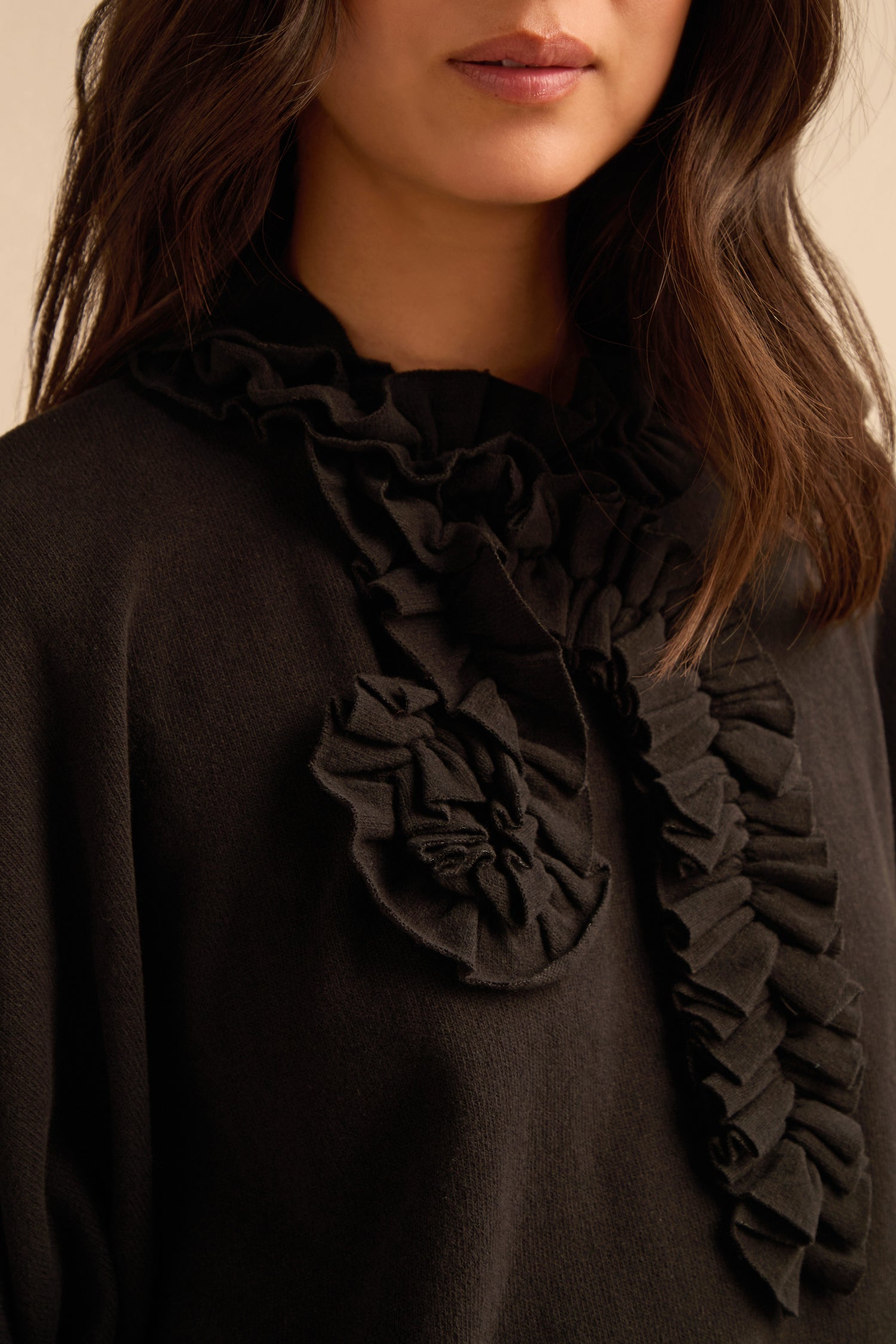 A woman wears the Black Frill Neck Top, featuring a ruffled collar and bow detail. Only her lower face, neck, and upper chest are visible. This elegant top is made in Italy.