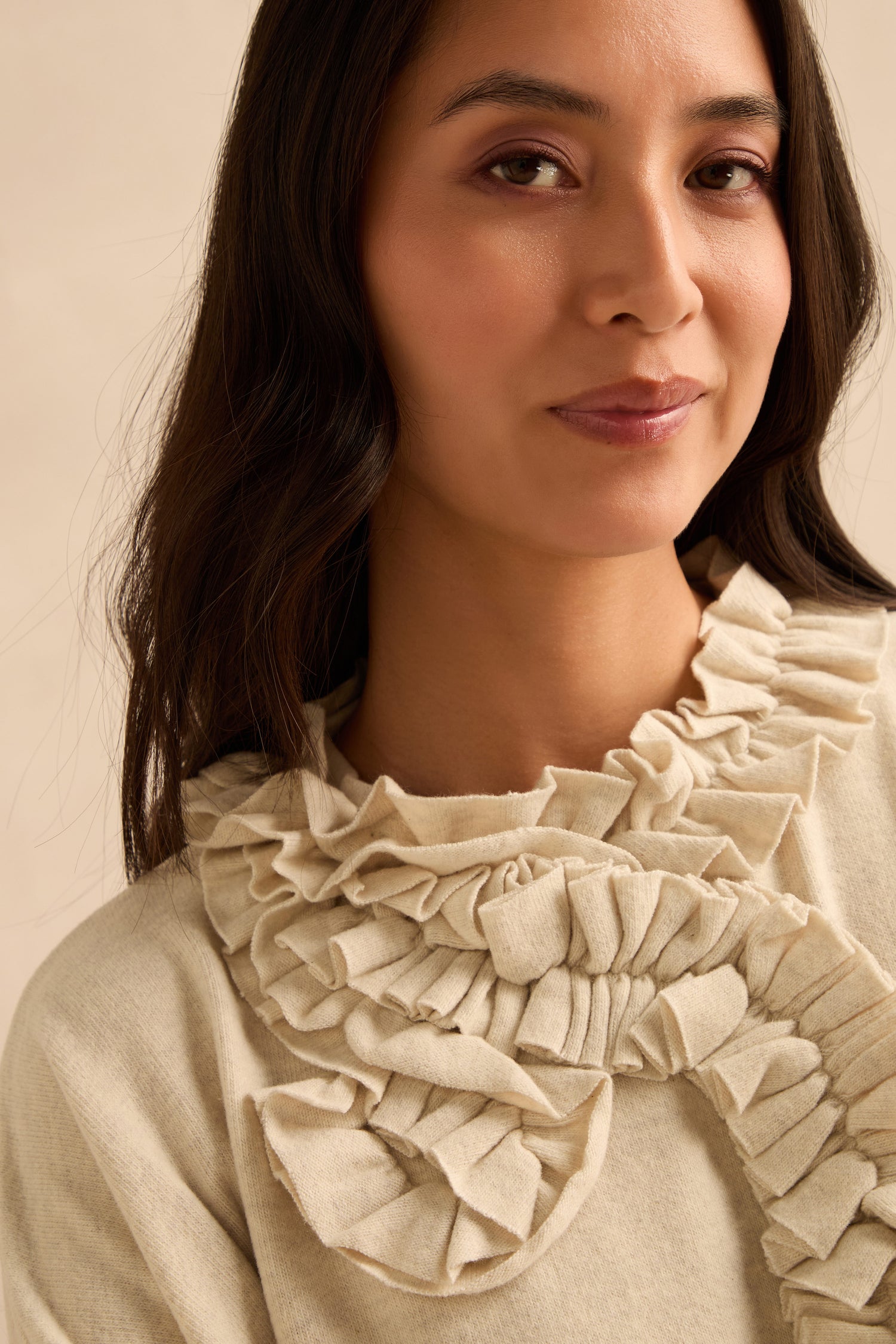 A woman with long dark hair wears the Cream Frill Neck Top, which features large, ruffled fabric details at the neckline and a relaxed boxy fit.