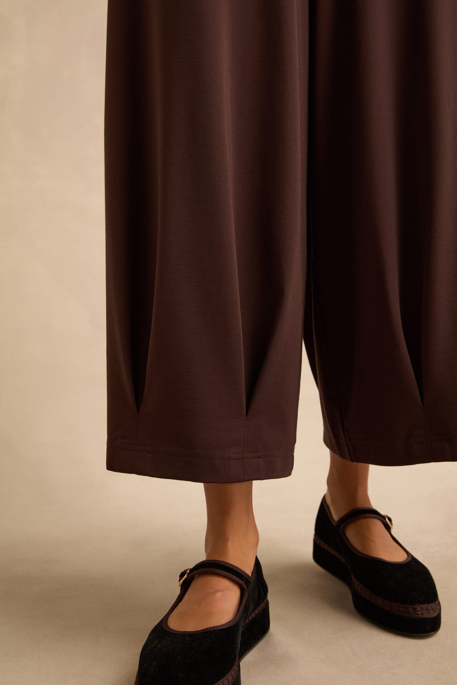 Chocolate Pleated Hem Wide Jersey Trousers in dark brown with pleated hems and a cropped length, worn with black Mary Jane shoes.