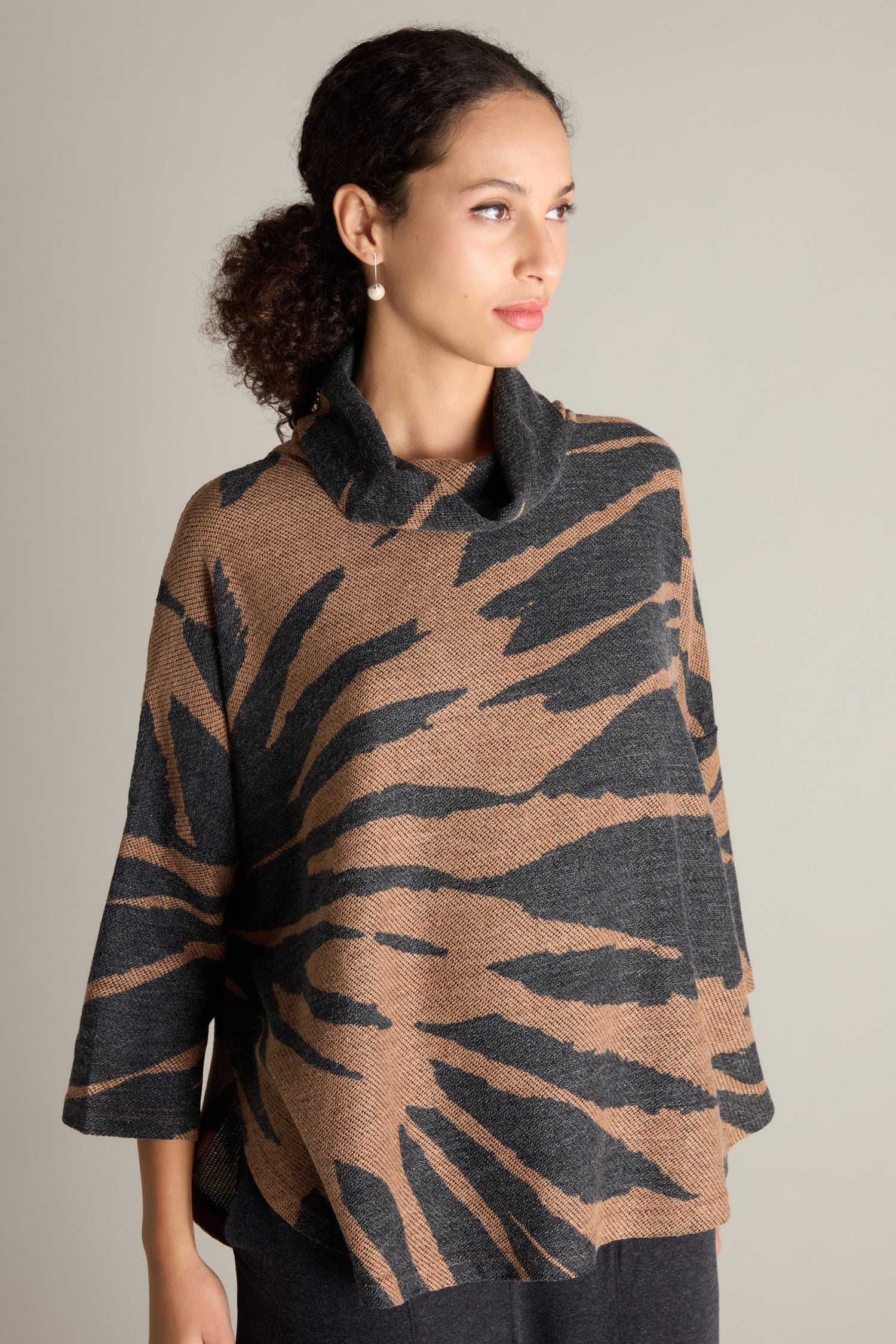 A person with curly hair wears a Cowl Neck Jacquard Top in a brown and black pattern made from luxe jacquard fabric. They are looking to the side against a neutral background.