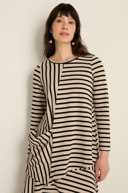Woman in an Asymmetric Stripe Jersey Tunic with long sleeves and a draped hem, made from soft viscose jersey, poses against a plain light-colored wall.