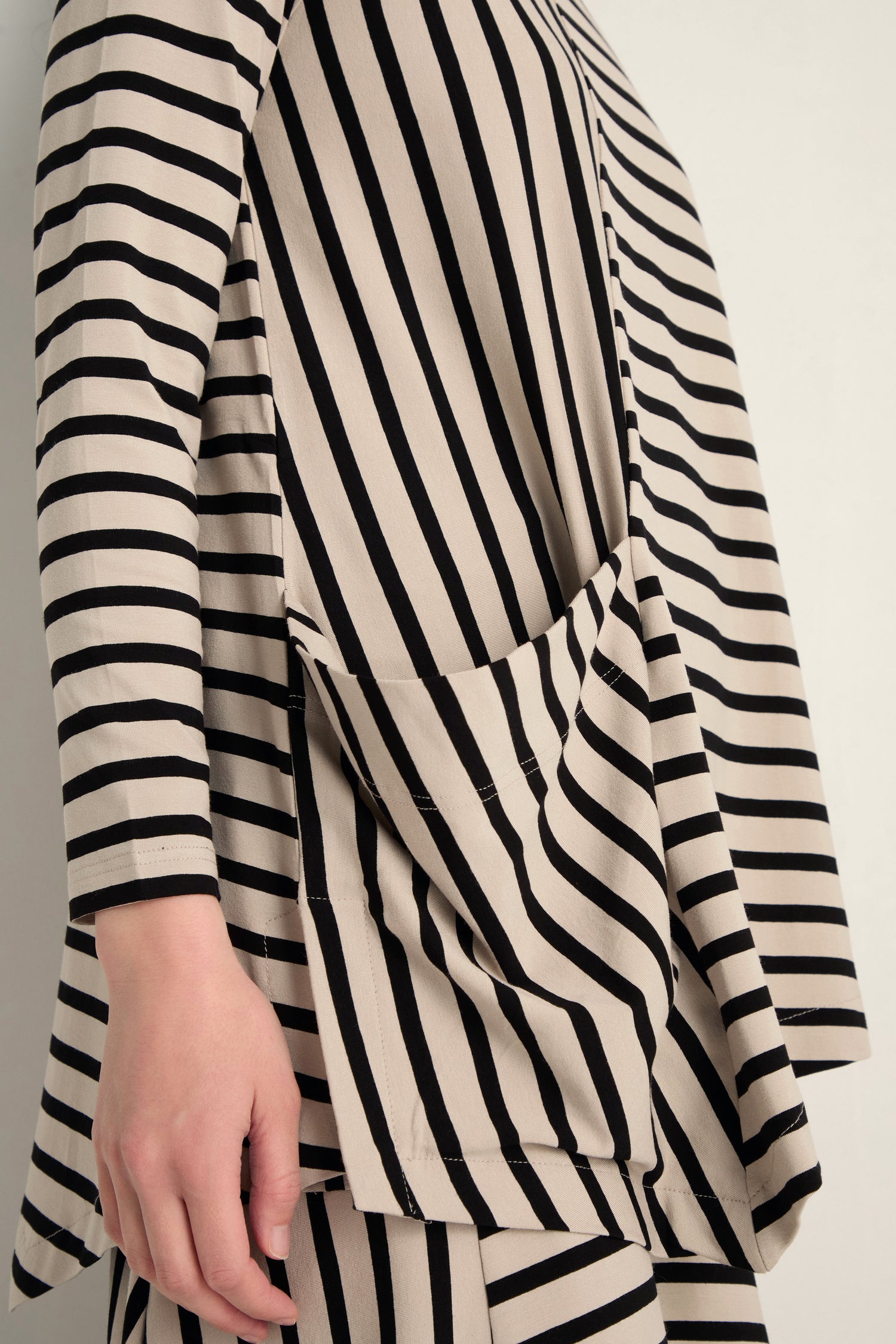 A person models the Asymmetric Stripe Jersey Tunic—a long-sleeved, beige top made from soft viscose jersey—set against a neutral background.