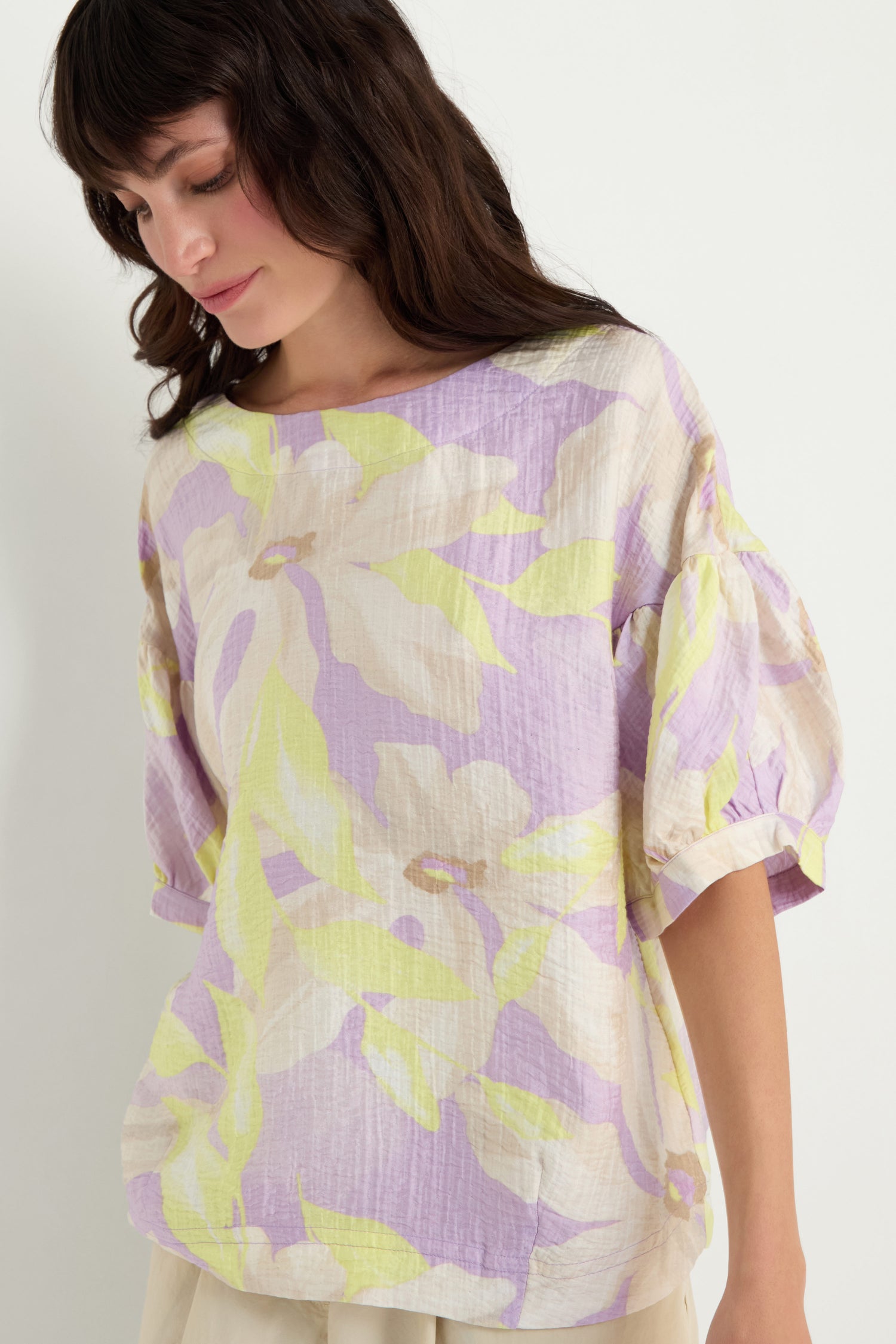 A woman wears the Puff Sleeve Print Top, featuring a relaxed fit and pastel floral print, as she looks down against a plain white background.