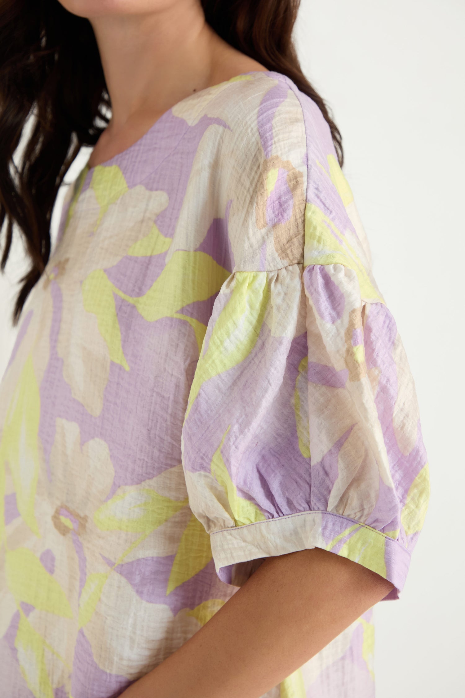 A woman wears the Puff Sleeve Print Top, a relaxed fit with pastel floral print in lavender, yellow, and cream on soft viscose blend, featuring short puff sleeves.