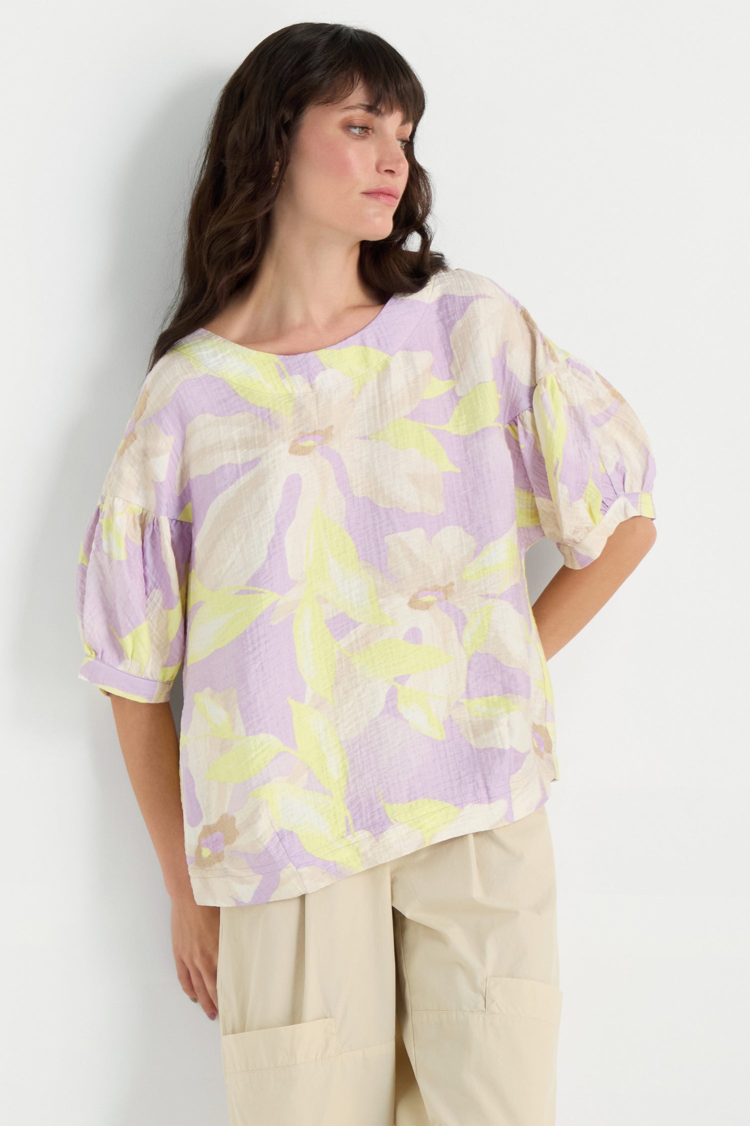 A woman in a Puff Sleeve Print Top, featuring a relaxed fit, pastel floral design, soft viscose blend, elbow-length puff sleeves, and beige pants stands against a plain white background.