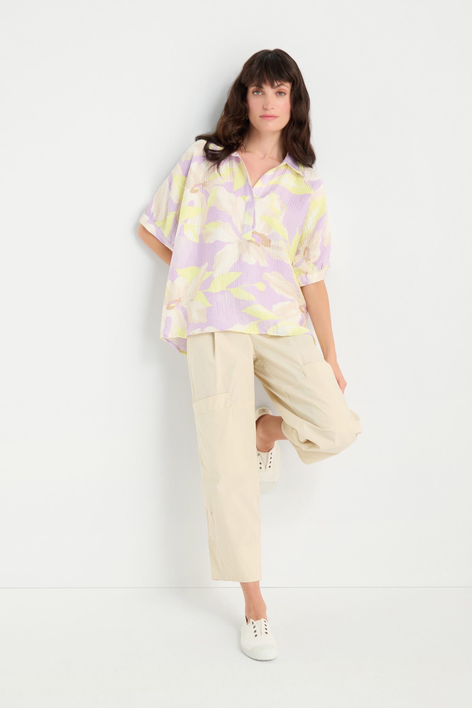 A woman wears the Print Collar Top, a relaxed fit pastel-patterned blouse, with beige pants and white sneakers, posing against a plain white background with one leg bent.