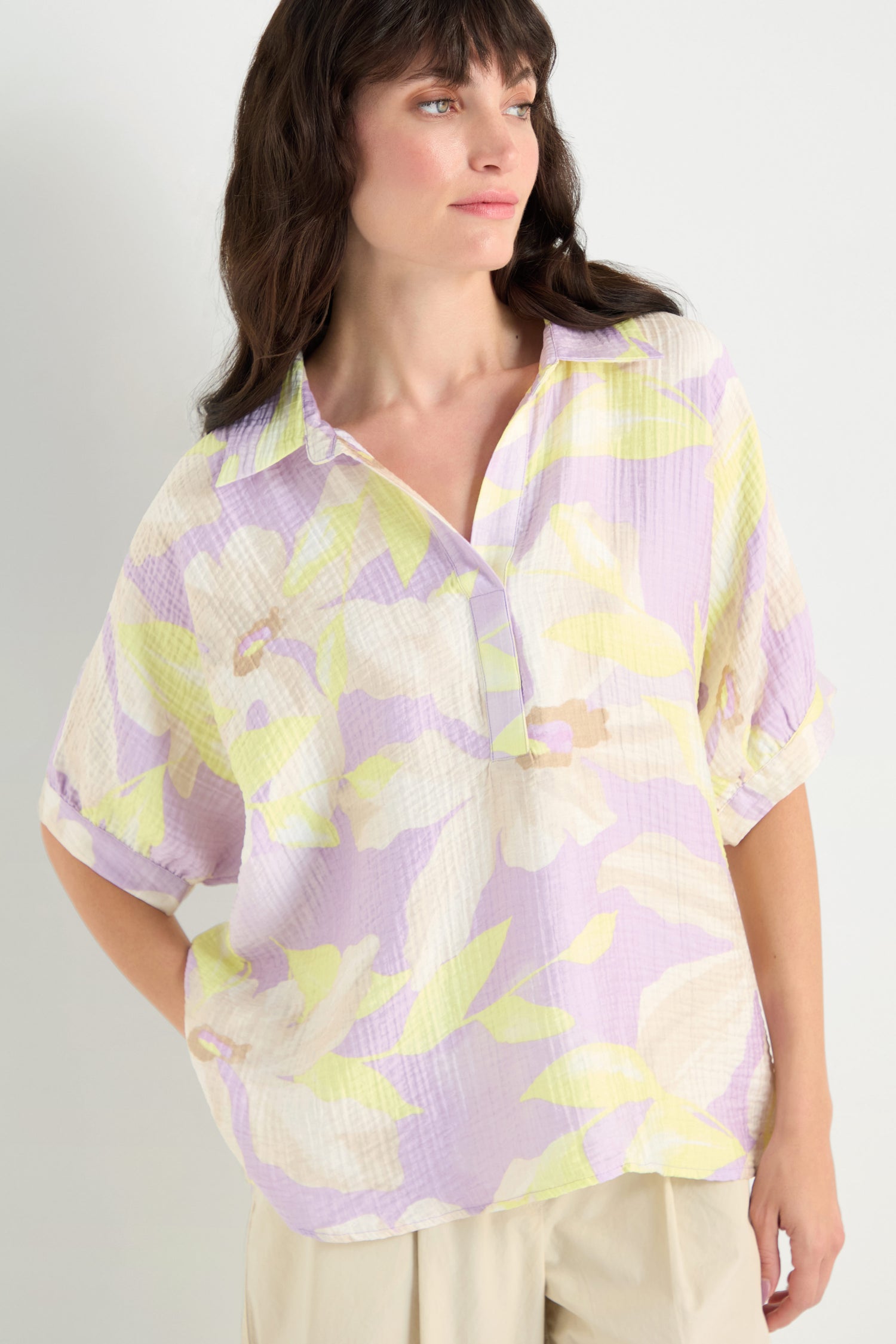 Woman wearing the Print Collar Top, a relaxed fit pastel floral viscose blend with rolled sleeves, paired with beige pants and standing against a plain light background.