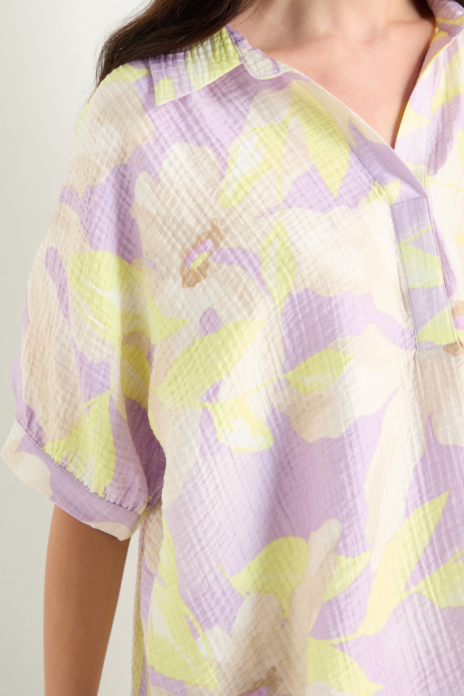 Close-up of a person wearing the Print Collar Top, a light viscose blend blouse with a pastel yellow, lilac, and cream floral pattern. It features short sleeves, a V-neckline, and a relaxed fit.