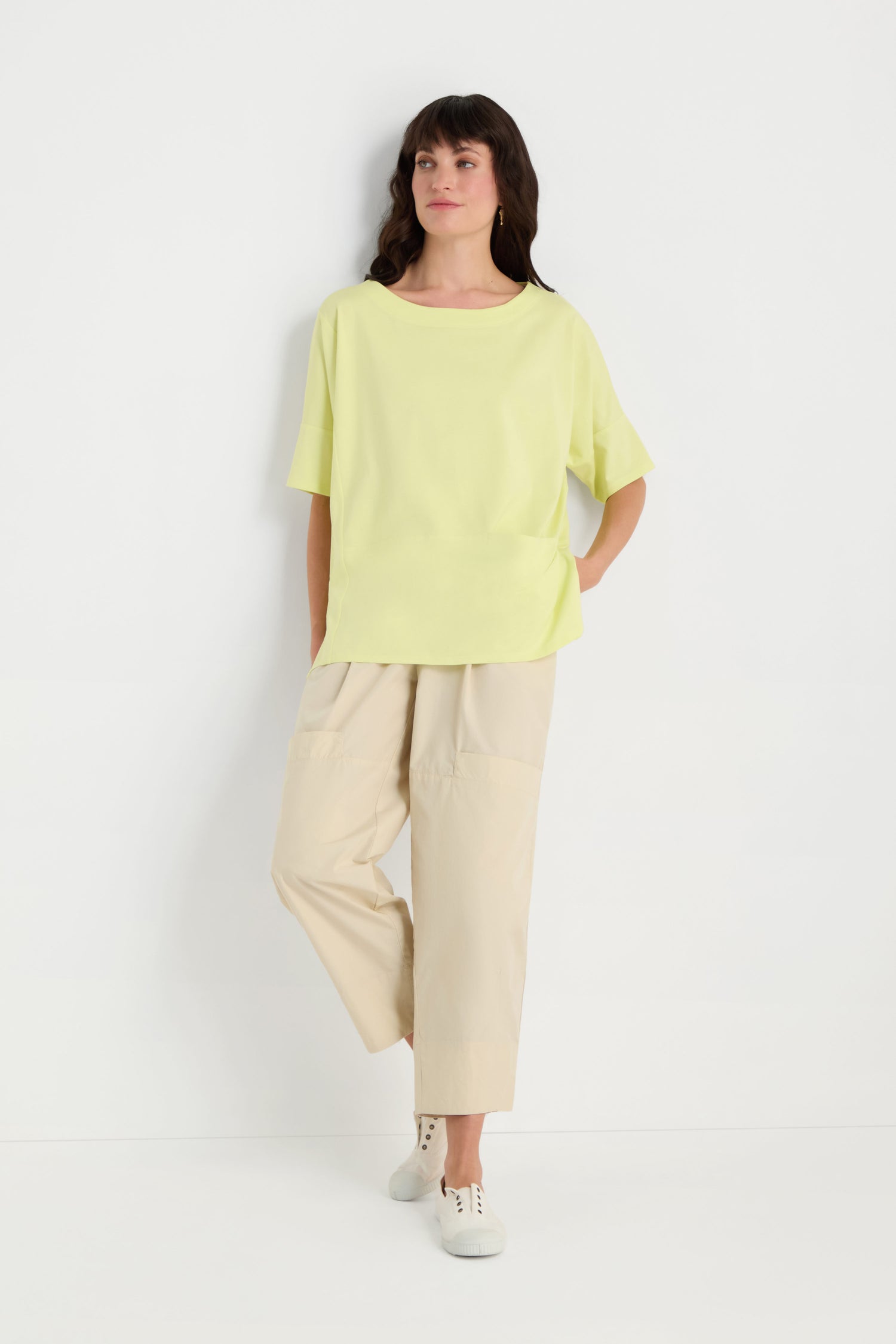 A woman stands against a white background wearing a relaxed fit Jersey Pocket Top in light yellow, paired with beige wide-leg pants and white sneakers.