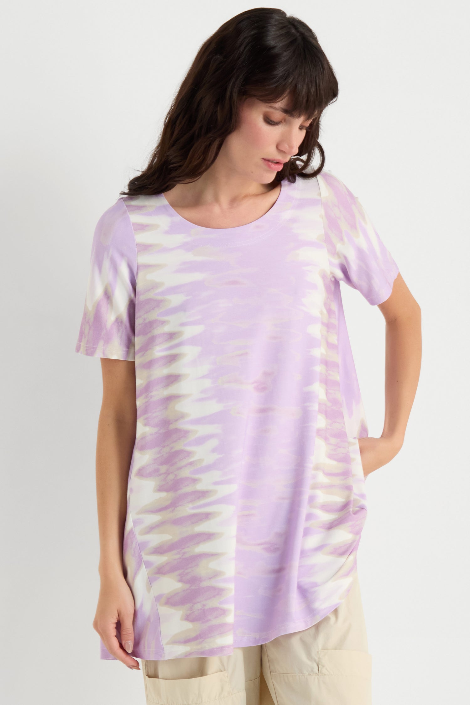 A woman models the Tie-Dye Jersey Tunic in light purple and white with a relaxed fit, paired with beige pants and posed against a plain white background.