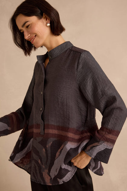 A woman poses against a plain beige background wearing the Print Hem Pocket Shirt—a relaxed fit, long-sleeved button-up with a wide collar and abstract border print.