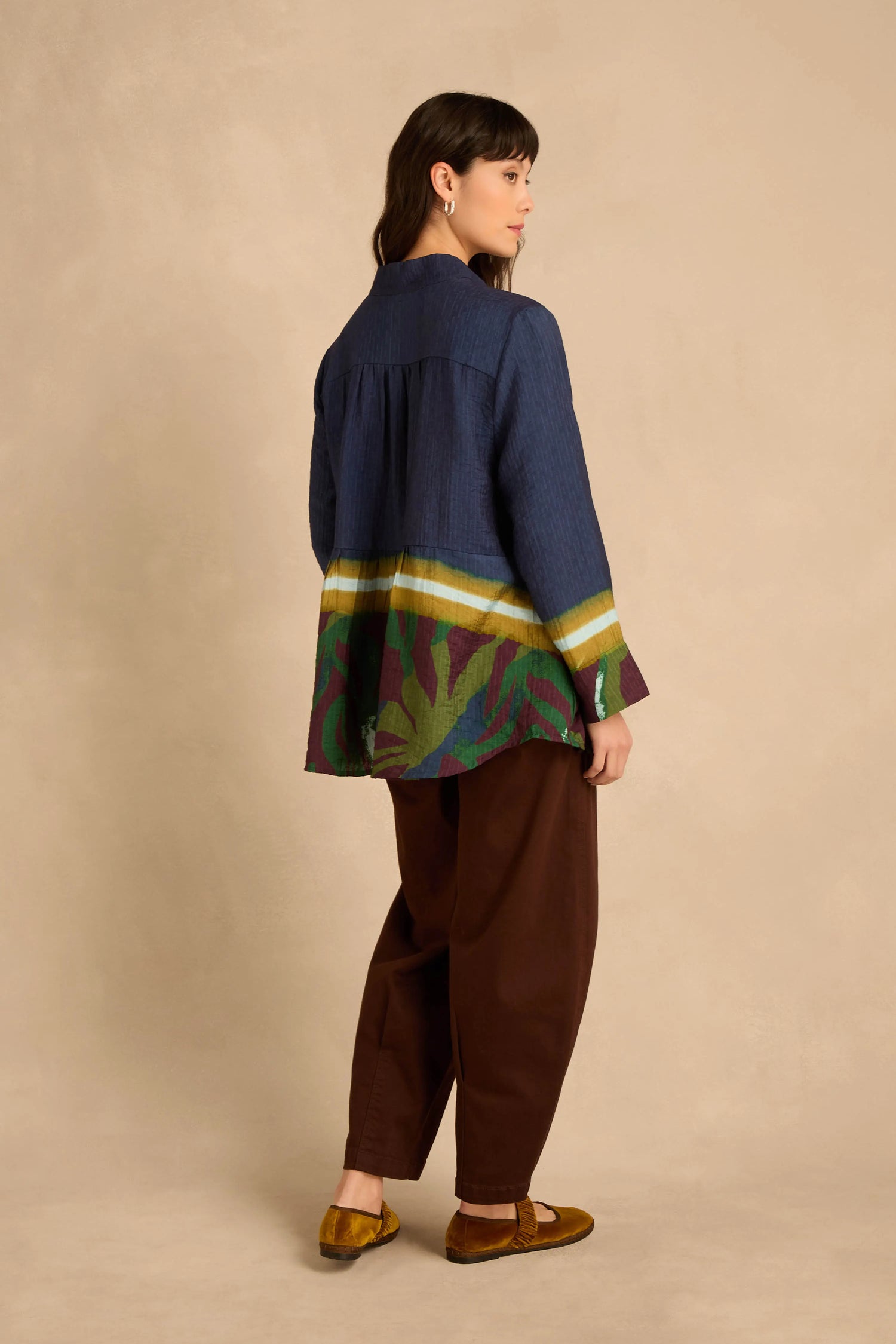 A person wearing a relaxed navy blue Print Hem Pocket Shirt with a decorative printed panel, paired with dark brown trousers and olive green flats.