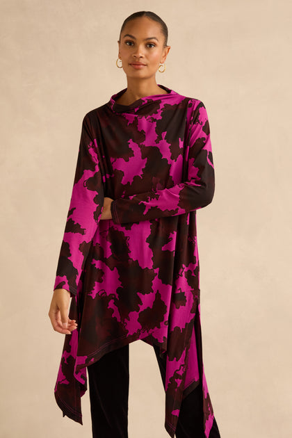 A person wearing an Autumn Leaves tunic featuring a magenta and dark brown abstract botanical print and an asymmetric hem over black leggings.