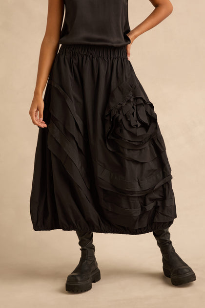 A person wearing a black sleeveless top, a Taffeta Bubble Skirt with large gathered rosettes, and black platform boots.