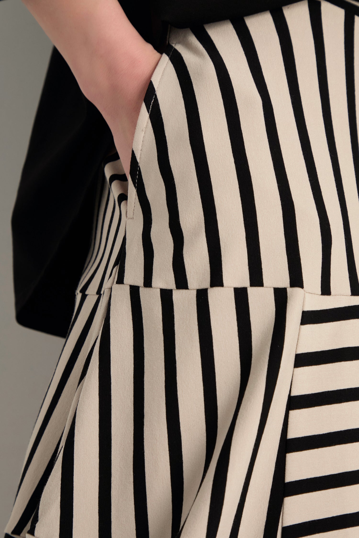 A close-up of a person wearing a black top and the Stripe Jersey Bubble Skirt in cream with black vertical and horizontal stripes, one hand casually tucked into the skirt's pocket.