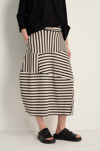 Person wearing a black top, black sandals, and the Stripe Jersey Bubble Skirt—midi length with black horizontal and vertical stripes—standing against a plain light background.