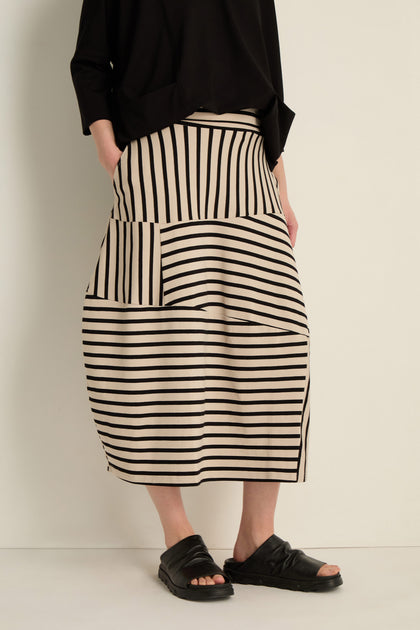 Person wearing a black top, black sandals, and the Stripe Jersey Bubble Skirt—midi length with black horizontal and vertical stripes—standing against a plain light background.