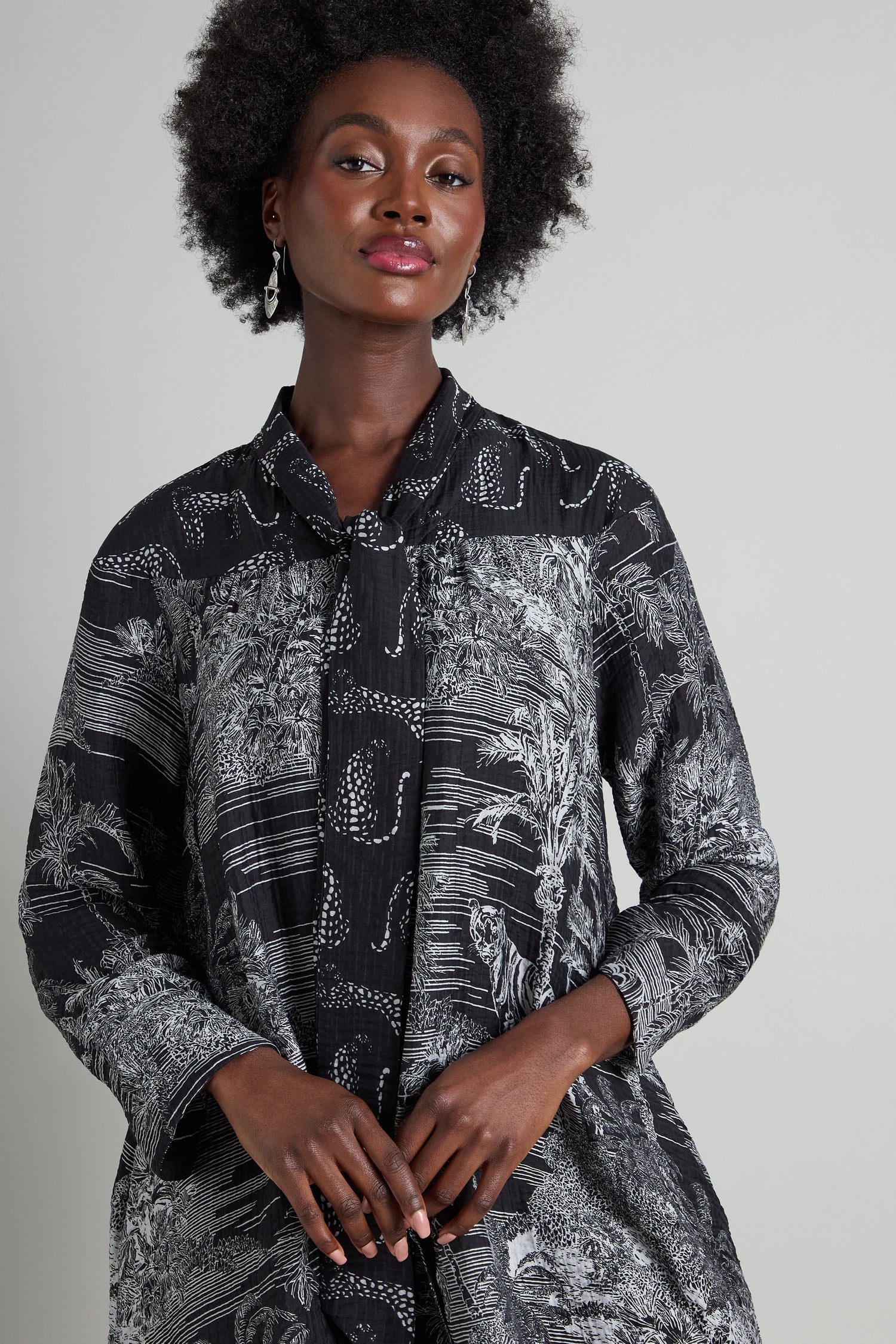 A person wearing the Tie Neck Viscose Shirt by Noen, showcasing a patterned black and gray design, poses elegantly against a plain background.