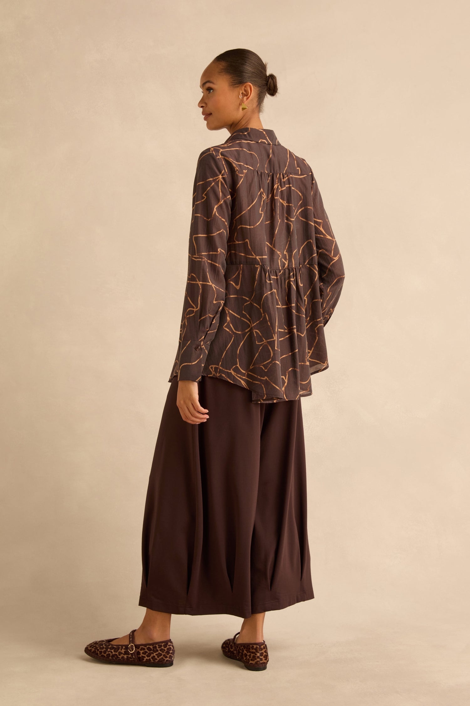 A person seen from behind wears a brown Swirl Print Sheer Shirt, a dark brown skirt, and leopard-print flat shoes.