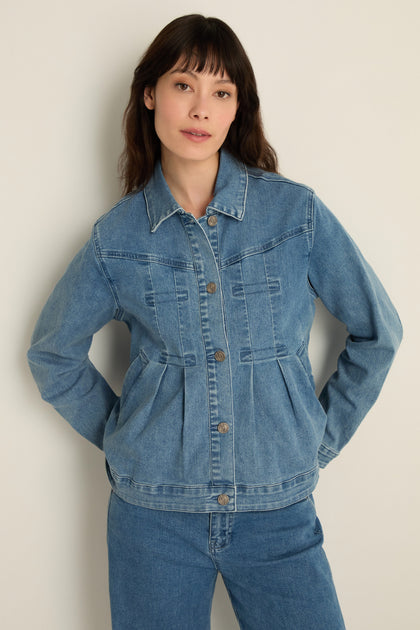 A woman stands against a plain light background wearing the Cropped Denim Jacket in stretch cotton denim and matching jeans—a perfect contemporary layer—with her hands behind her back.