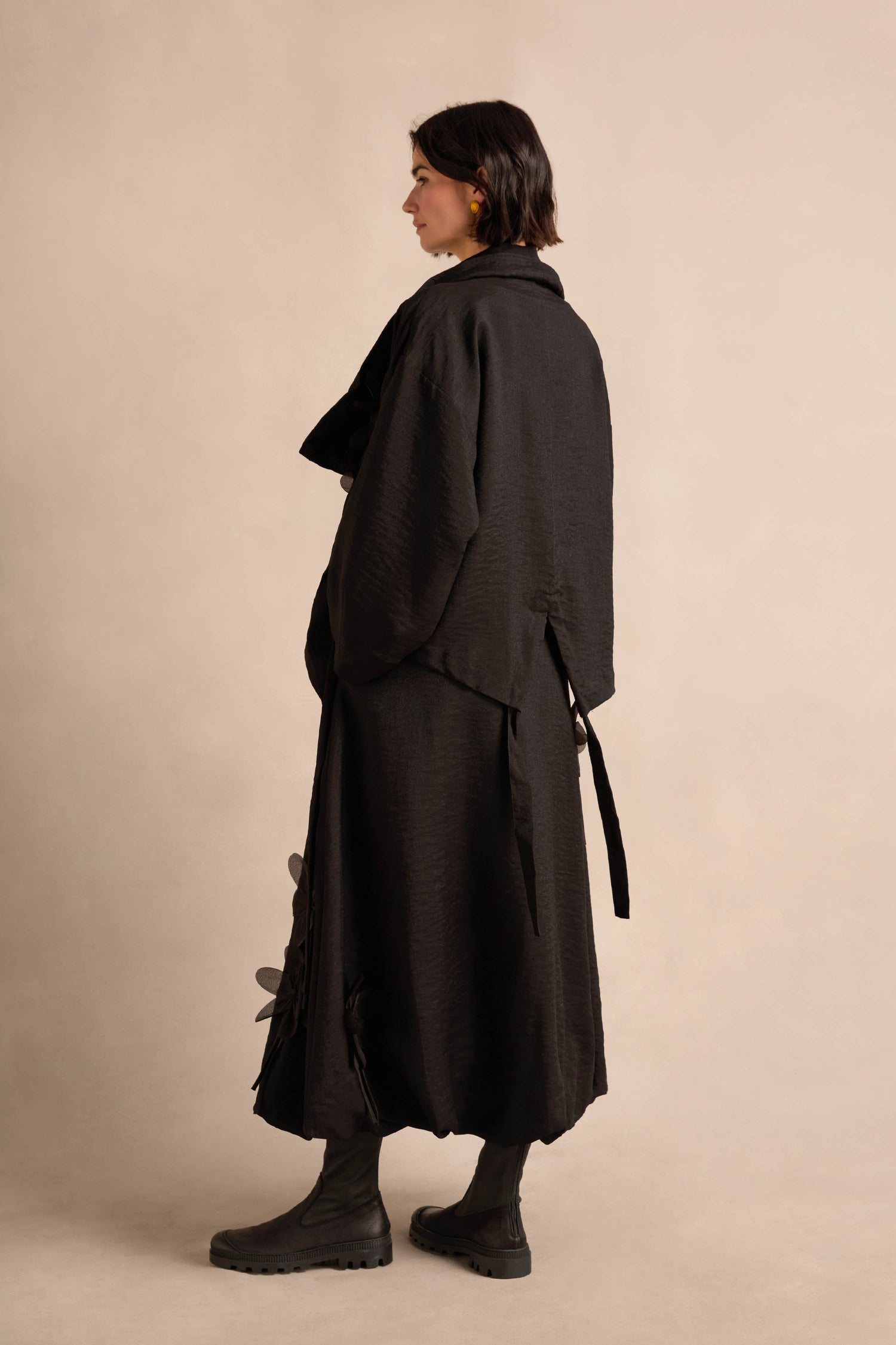 A person models the Flower Detail Jacket, standing sideways against a neutral background and pairing it with black boots.