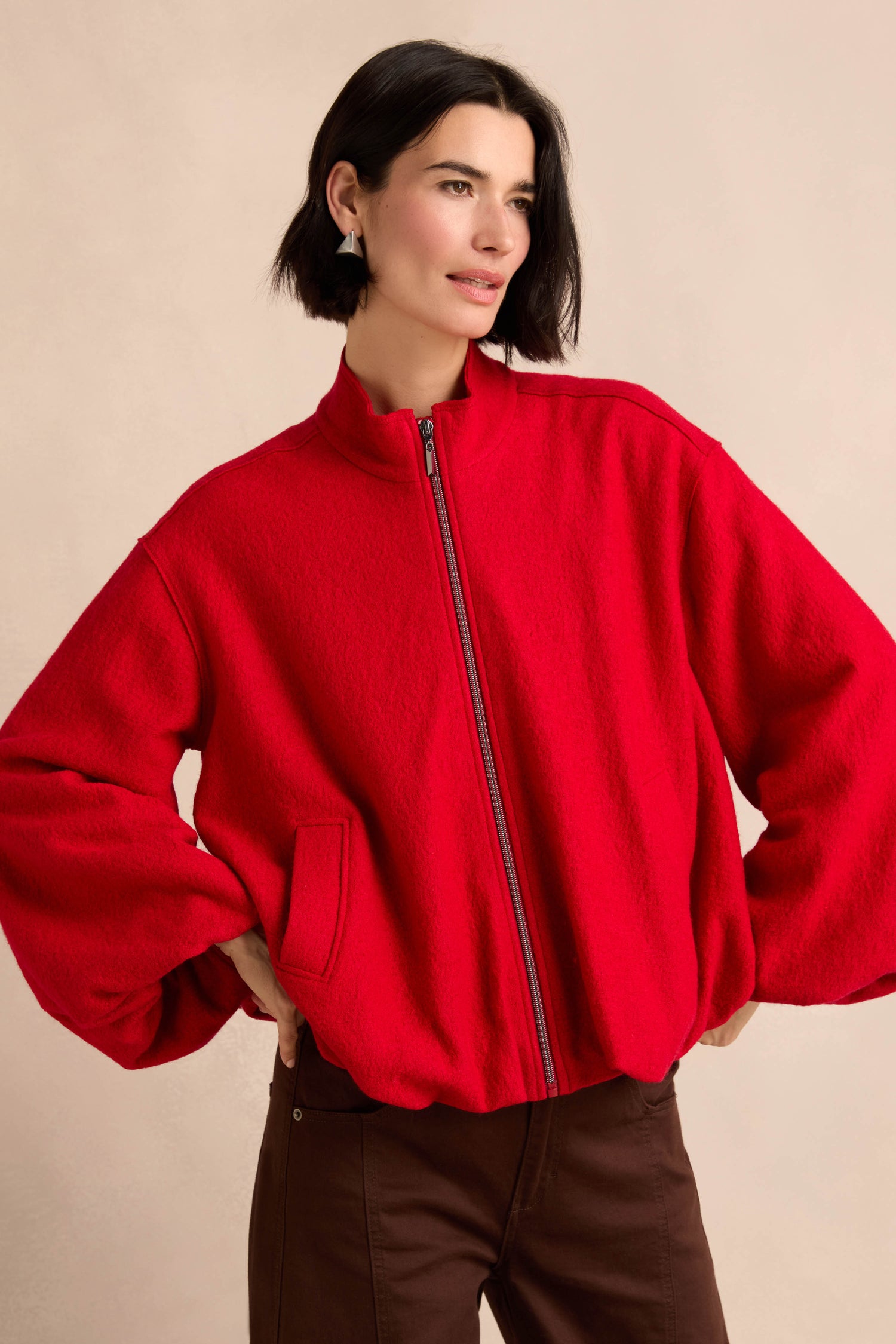 A person wearing the Puffball Boiled Wool Jacket in bright red and brown pants stands with hands in pockets against a neutral background.