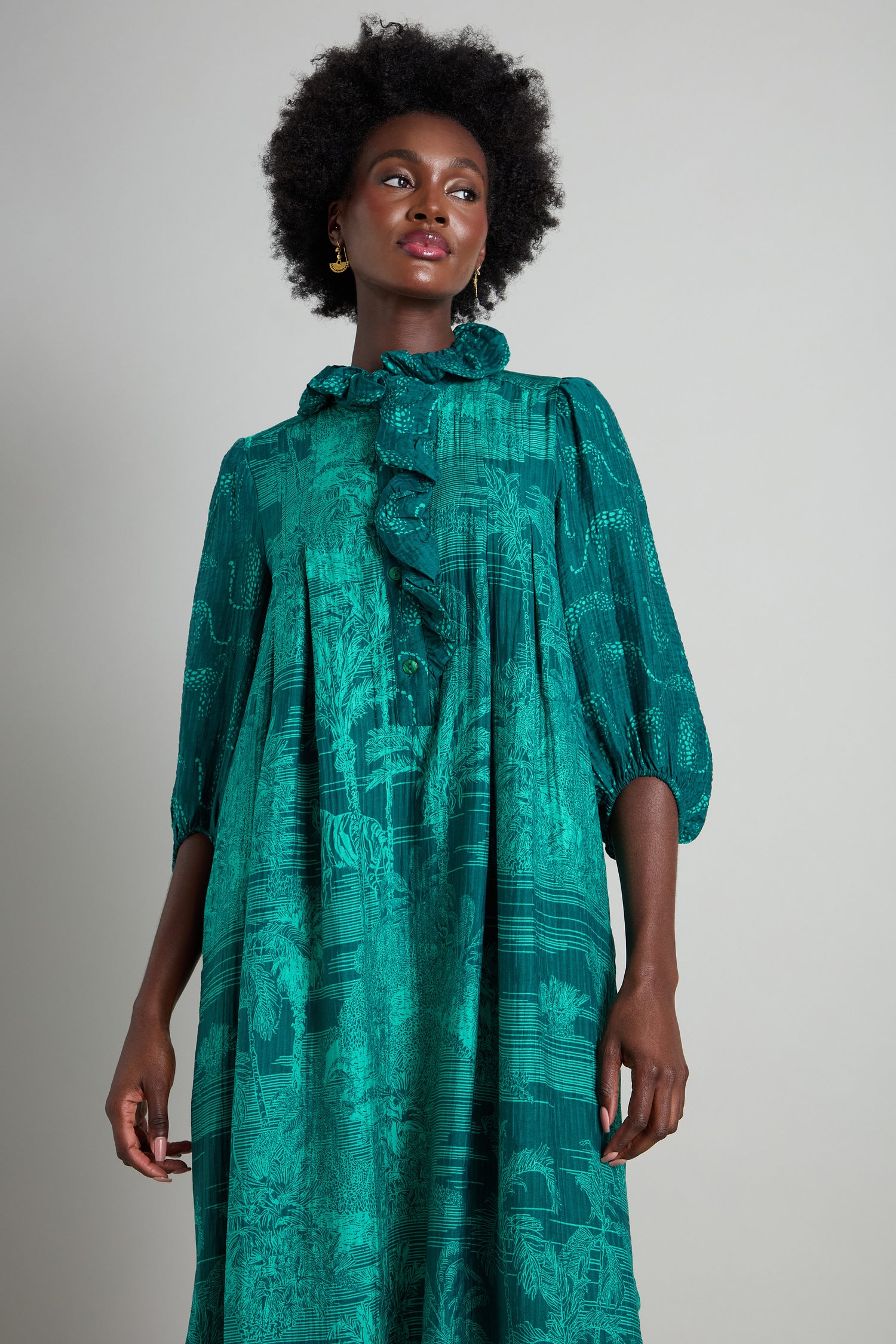 Person wearing the Frill Neck Viscose Dress, featuring a green, jungle-inspired print with a ruffled collar and quarter-length sleeves, standing against a plain backdrop.