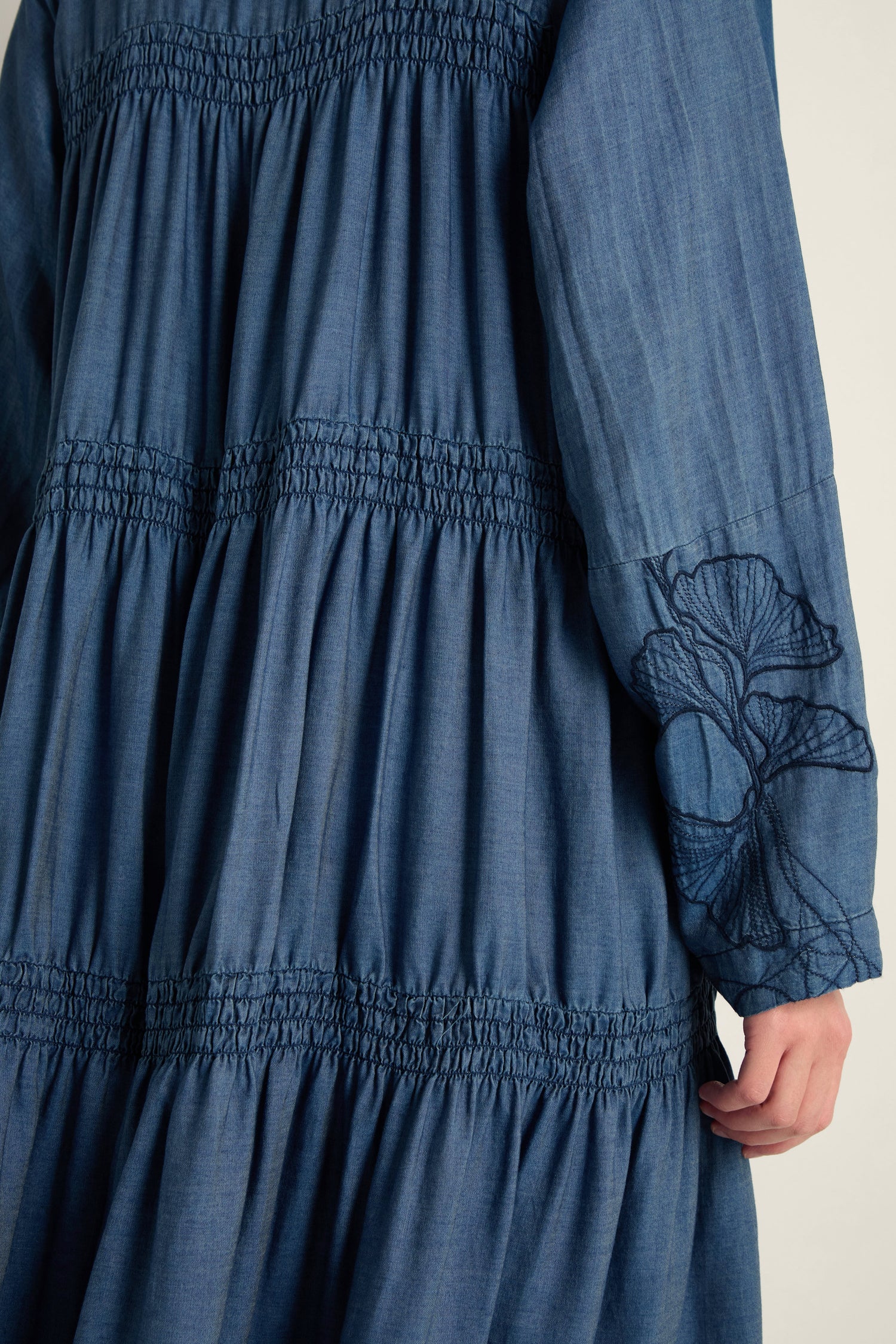 Close-up of the Ginkgo Embroidered Denim Dress in blue, featuring midi length, gathered and ruched details, and delicate floral embroidery on the lyocell denim sleeves.